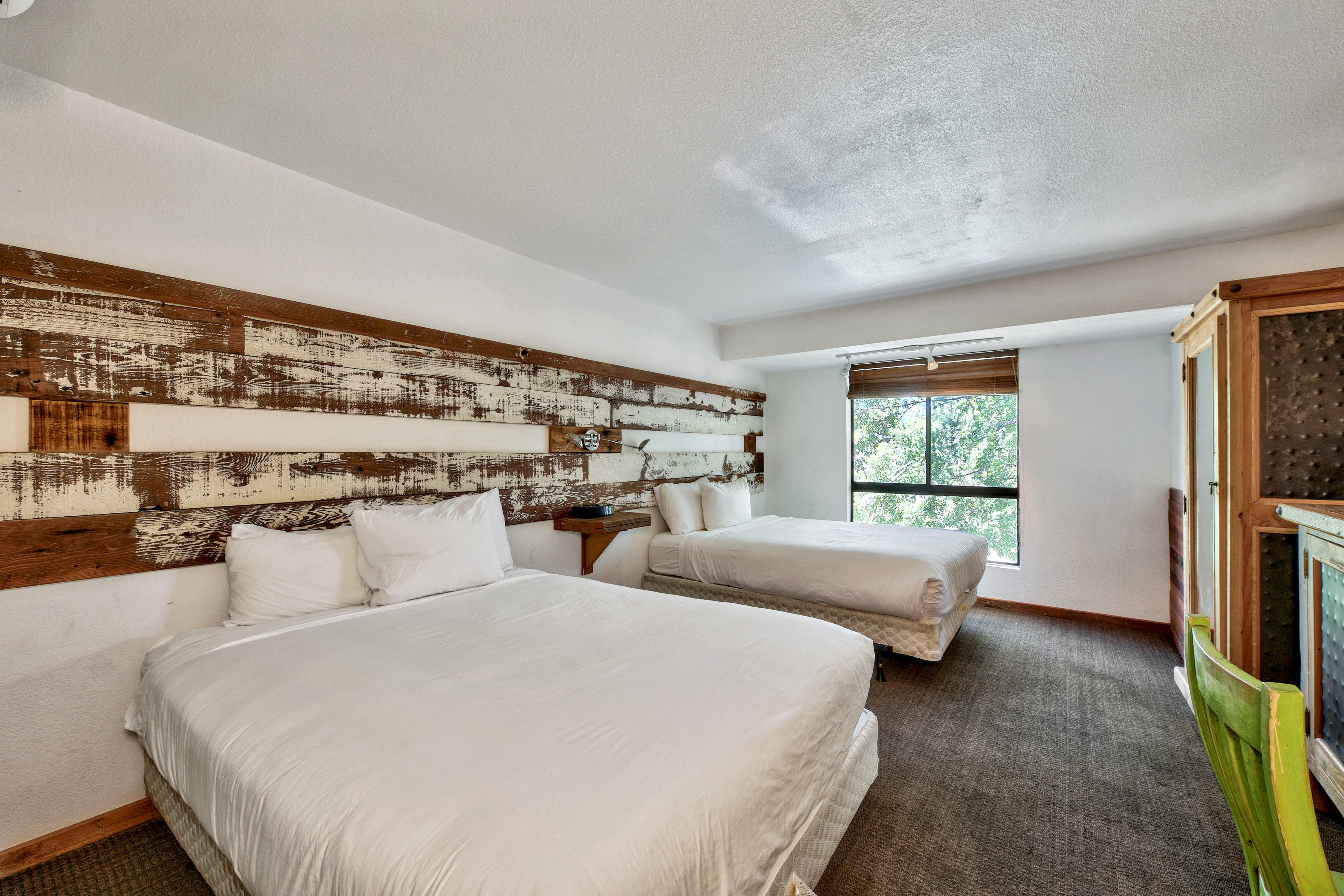 A hotel room with two beds, a wooden headboard, and a window.