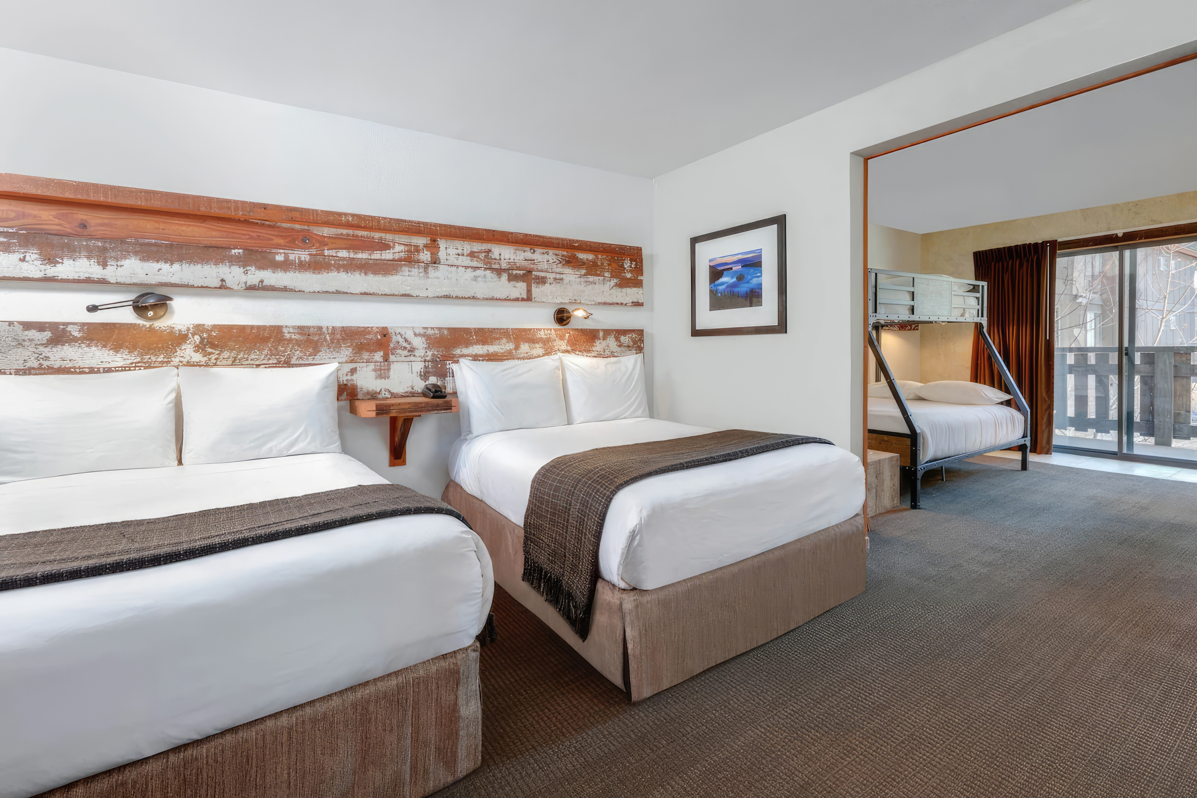 A hotel room with two twin beds and a bunk bed in the background.