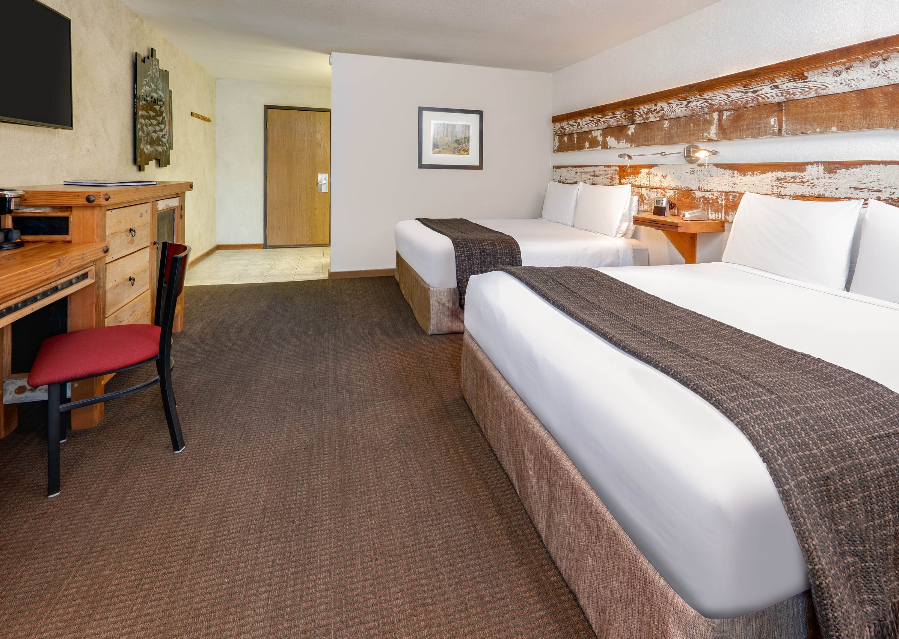 A hotel room with two queen beds, a desk, and a TV on the wall.